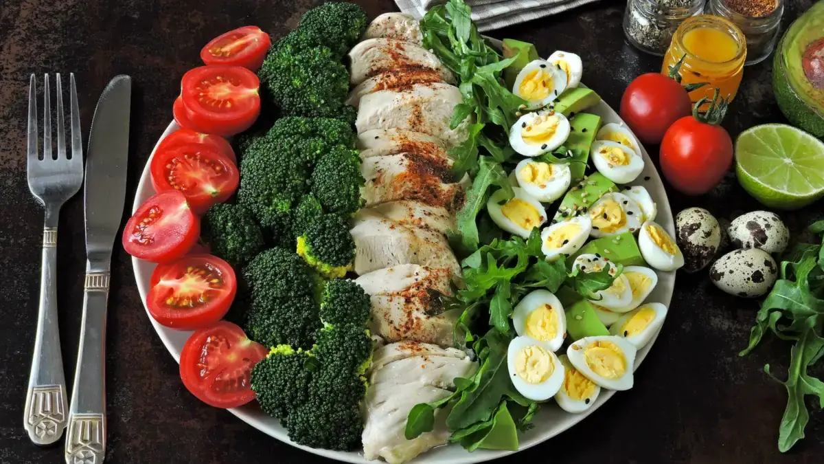 A plate of chicken, broccoli, eggs, tomato and salad