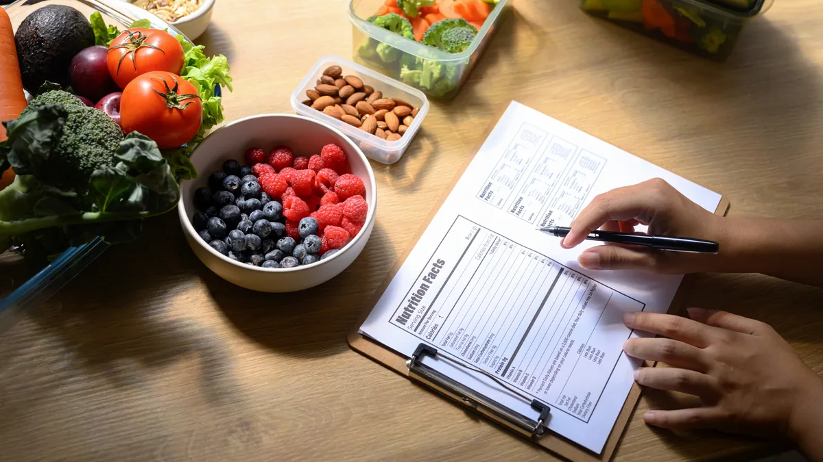 Hands filling in a food diary next to fruit and vegetables